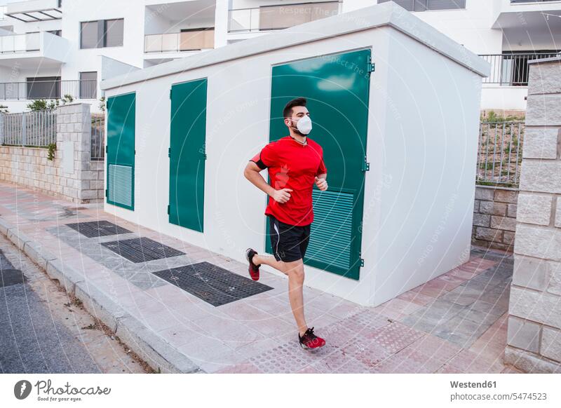 Mittelgroßer erwachsener Mann mit Gesichtsmaske beim Laufen auf einem Fußweg in der Stadt Farbaufnahme Farbe Farbfoto Farbphoto Spanien Außenaufnahme außen