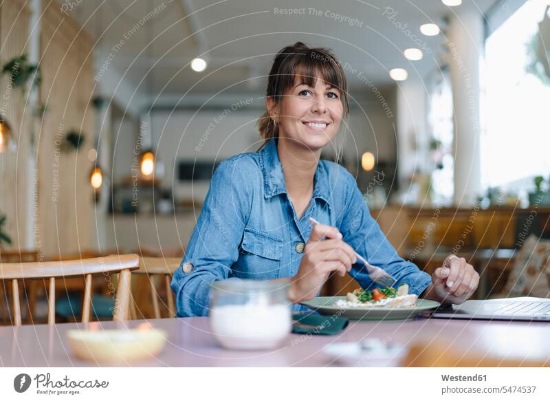 Weiblicher Besitzer isst Essen, während er im Cafe sitzt Farbaufnahme Farbe Farbfoto Farbphoto Innenaufnahme Innenaufnahmen innen drinnen Tag Tageslichtaufnahme