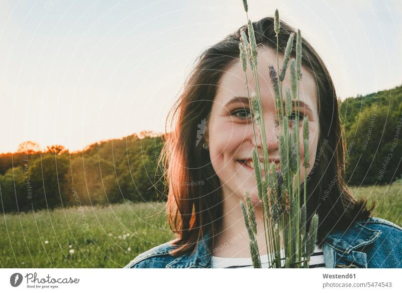 Porträt eines lächelnden Teenager-Mädchens mit Gräsern bei Sonnenuntergang abends sommerlich Sommerzeit freuen zufrieden auf dem Land auf dem Lande Muße Flora