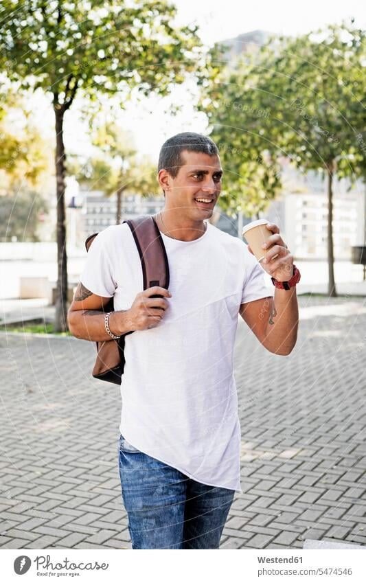 Lächelnder junger Mann mit Kaffee zum Mitnehmen auf dem Weg lächeln Männer männlich unterwegs auf Achse in Bewegung Erwachsener erwachsen Mensch Menschen Leute