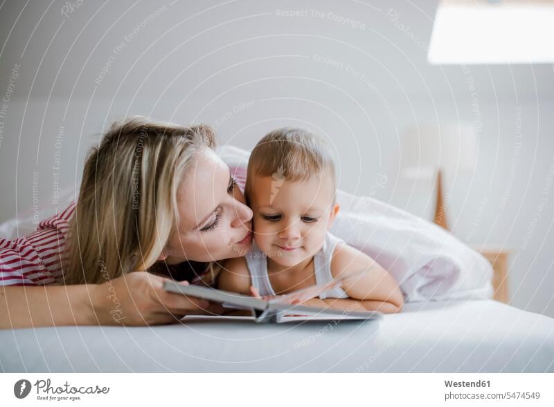 Mutter küssen Kleinkind Sohn im Bett liegend zu Hause ein Buch lesen Zuhause Eltern Familie Mensch Kind bequem Pyjama ausruhen Bauchlage Kindheit Gemeinsamkeit