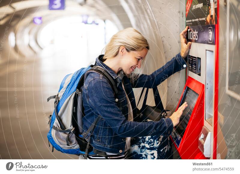 Lächelnde Frau mit Fahrkartenautomat am Bahnhof Österreich Reisende Reisender Verkehr Fahrschein Ticket Pendler unterirdisch Aufbruch Jeansjacke Jeansjacken