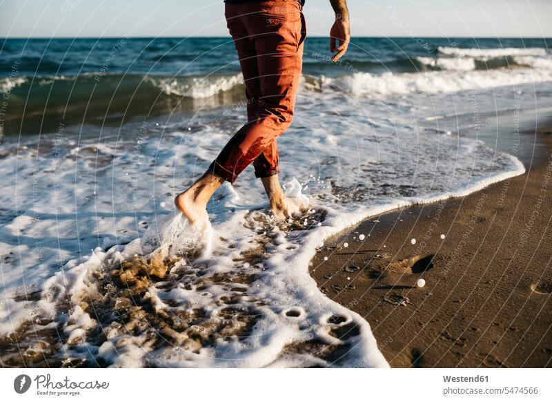 Rückansicht eines Mannes mit orangefarbener Hose, der an einem Strand am Wasser spazieren geht Leute Menschen People Person Personen Europäisch Kaukasier