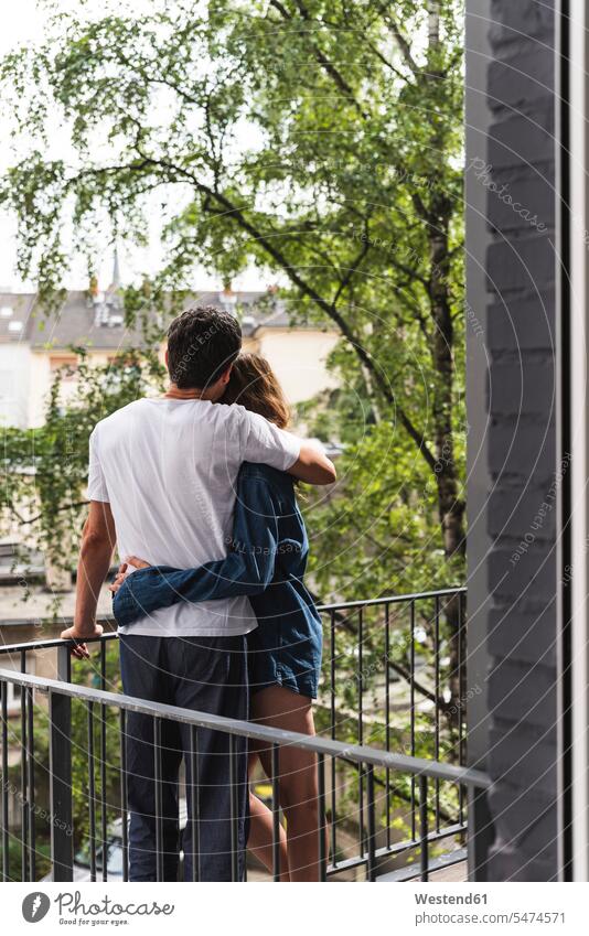 Rückansicht eines Paares in Nachtwäsche, das auf dem Balkon steht und sich umarmt stehen stehend Balkone Pärchen Partnerschaft Zuhause zu Hause daheim umarmen