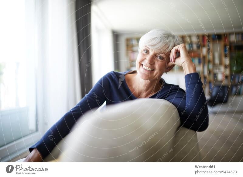 Lächelnde ältere Frau entspannt beim Sitzen auf dem Sofa Farbaufnahme Farbe Farbfoto Farbphoto Innenaufnahme Innenaufnahmen innen drinnen Tag Tageslichtaufnahme
