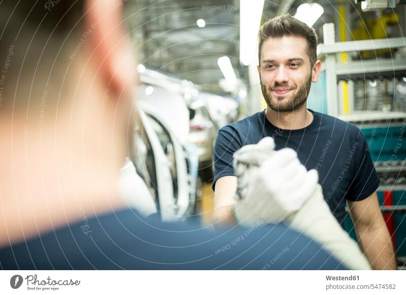 Zwei Kollegen schütteln sich in moderner Autofabrik die Hand Arbeitskollege Arbeitskollegen Job Berufe Berufstätigkeit Beschäftigung Jobs Arbeiter T-Shirts KFZ