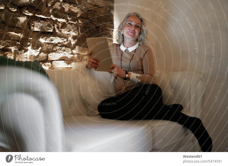 Porträt der glücklichen reifen Geschäftsfrau sitzt auf Couch mit digitalen Tablette Italien WLan Wireless Lan W-Lan Wifi Lichtschein Best Ager bestes Alter