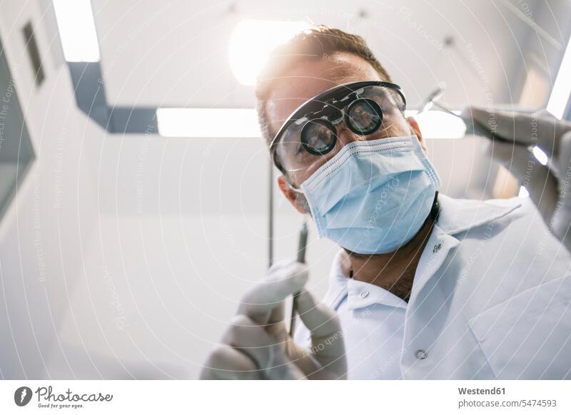 Männlicher Zahnarzt in chirurgischer Lupe und Maske mit medizinischen Instrumenten während der Behandlung in der Klinik Farbaufnahme Farbe Farbfoto Farbphoto