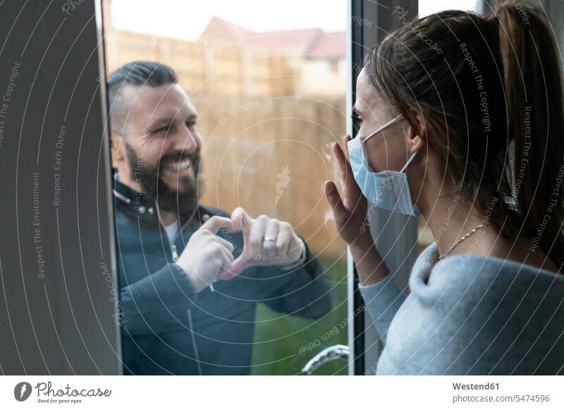 Freund zeigt herzförmige Geste gegenüber seiner Freundin durch Fensterglas während der COVID-19-Krise Farbaufnahme Farbe Farbfoto Farbphoto Tag