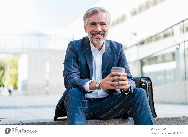 Porträt eines lächelnden reifen Geschäftsmannes, der auf einer Treppe in der Stadt sitzt und Kaffee zum Mitnehmen in der Hand hält Leute Menschen People Person