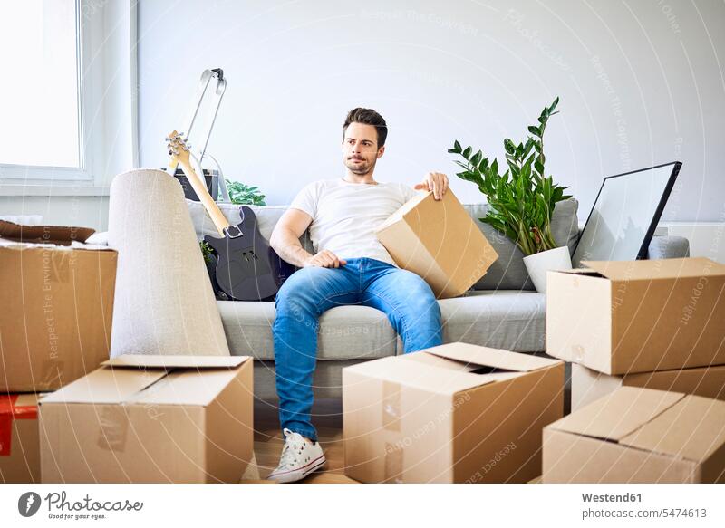 Frustrierter Mann sitzt auf Couch, umgeben von Pappkartons Frustration frustrierend frustriert Umzugskarton Umzugskiste Umzugskisten Umzugskartons sitzen