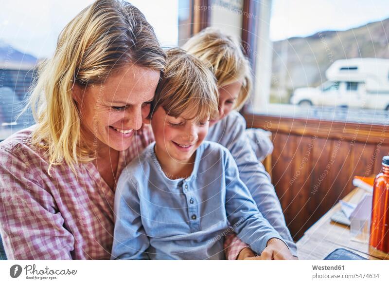 Glückliche Mutter mit zwei Söhnen sitzen am Tisch in einem Cafe Sohn Tische Kaffeehaus Bistro Cafes Café Cafés Kaffeehäuser Mami Mutti Mütter Mama sitzend sitzt
