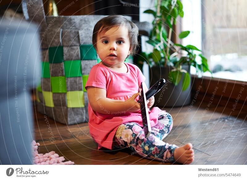 Porträt der niedlichen Baby-Mädchen sitzt auf dem Boden zu Hause hält Fernbedienung Fernbedienungen süss süß putzig Portrait Porträts Portraits weibliche Babys