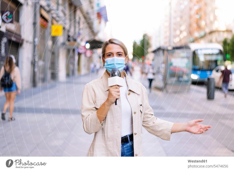 Reporterin mit Maske spricht über Mikrofon auf der Straße in der Stadt Farbaufnahme Farbe Farbfoto Farbphoto Spanien Außenaufnahme außen draußen im Freien Tag