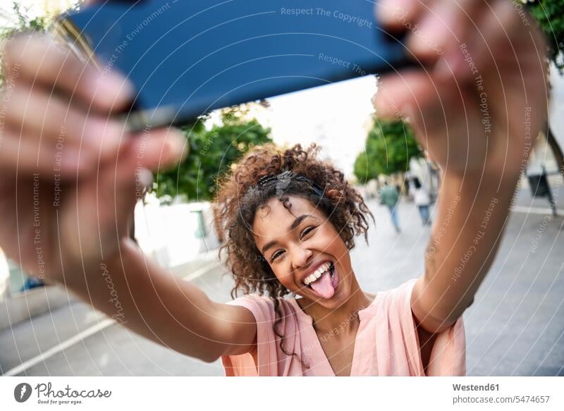 Unbekümmerte junge Frau macht ein Selfie in der Stadt staedtisch städtisch Selfies Unbeschwert Sorglos weiblich Frauen Außenaufnahme draußen im Freien