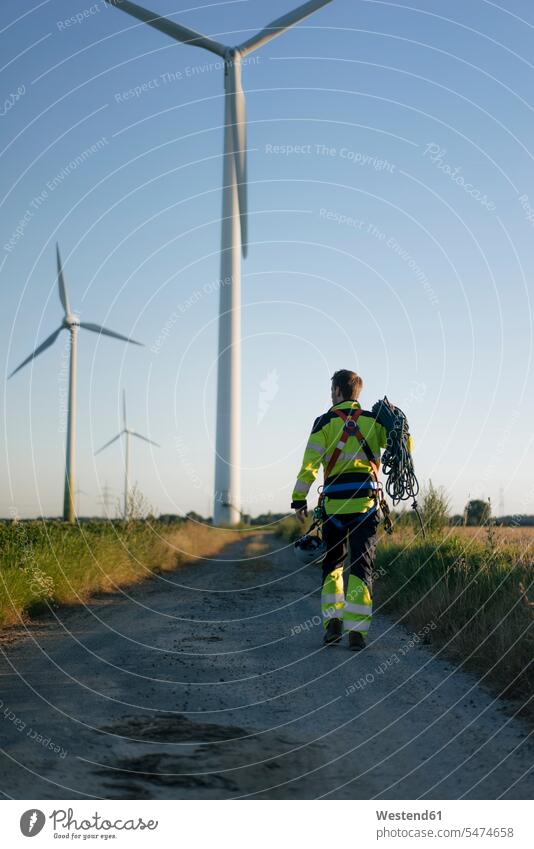 Techniker auf einem Feldweg in einem Windpark mit Kletterausrüstung gehen gehend geht Windenergieanlage WEA WEAs Windkraftwerk Windenergieanlagen Windkraftwerke
