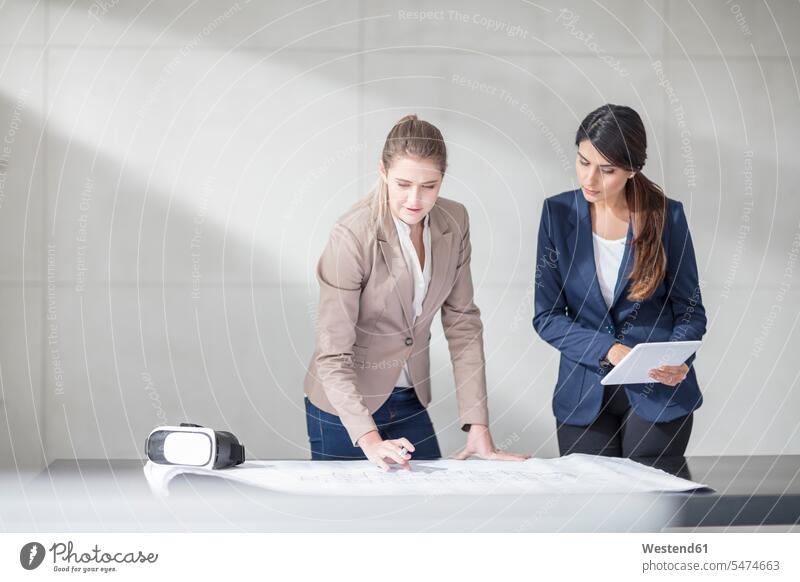 Zwei junge Frauen mit Tablett und VR-Brille arbeiten im Büro an der Blaupause Arbeit Tisch Tische Brillen Office Büros weiblich Bauplan Architekturplan