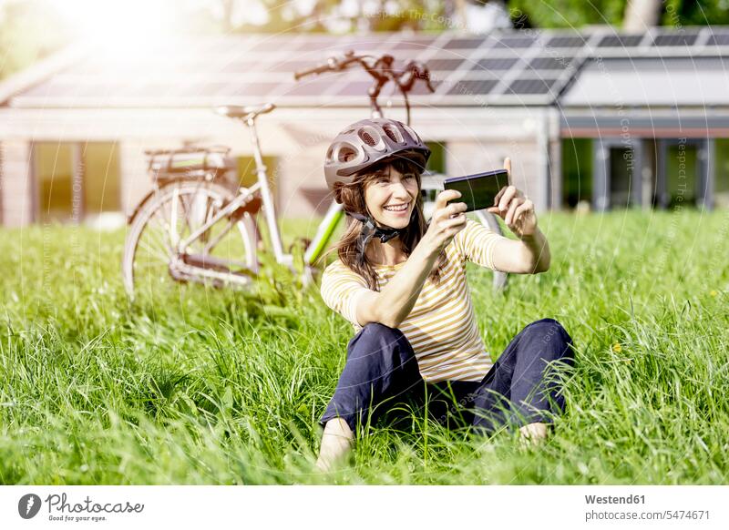 Glückliche Frau sitzt auf einer Wiese mit Fahrrad und macht ein Selfie Leute Menschen People Person Personen Europäisch Kaukasier kaukasisch 1 Ein ein Mensch