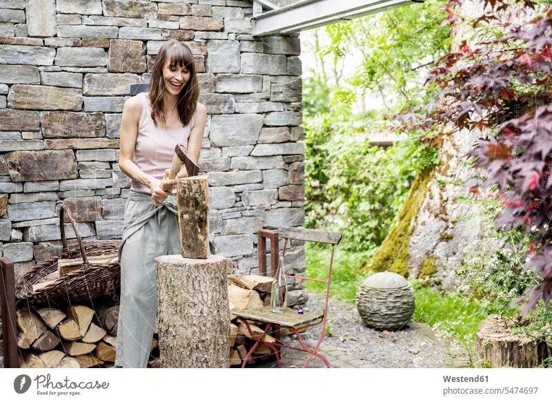 Schreiende Frau hackt Holz vor einem Haus Leute Menschen People Person Personen Europäisch Kaukasier kaukasisch 1 Ein ein Mensch nur eine Person single