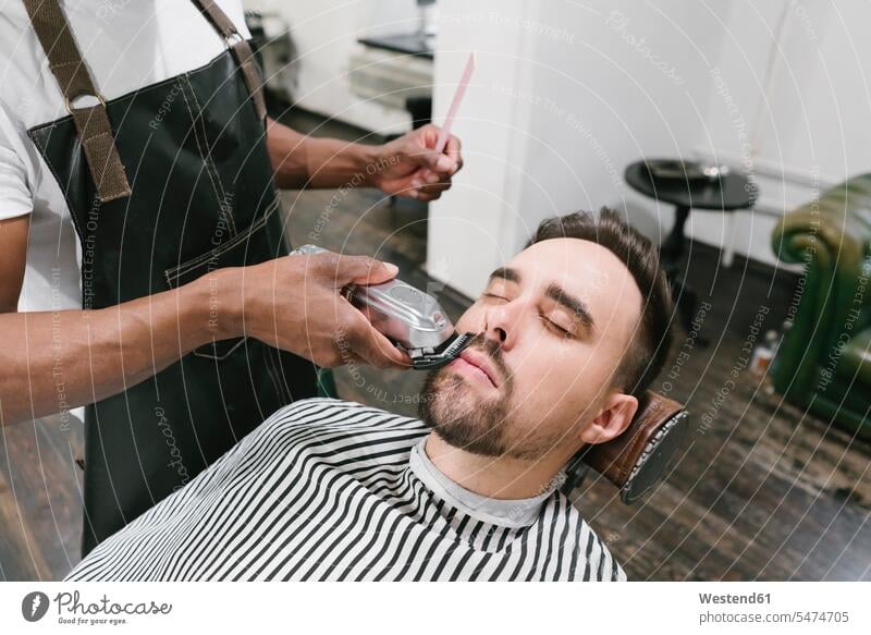 Barbier schneidet den Bart eines Kunden im Friseurladen Leute Menschen People Person Personen Afrikanisch Afrikanische Abstammung dunkelhäutig Farbige Farbiger