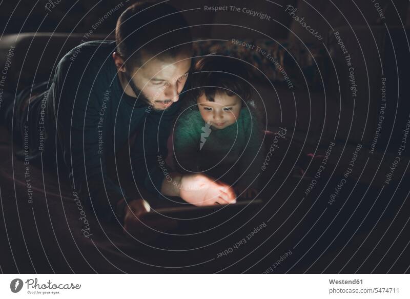 Vater und Tochter schauen sich zu Hause im Dunkeln ein digitales Tablet an Väter Papa Vati Familienvater Papi Baby Babies Babys Säuglinge Kind Kinder sehend