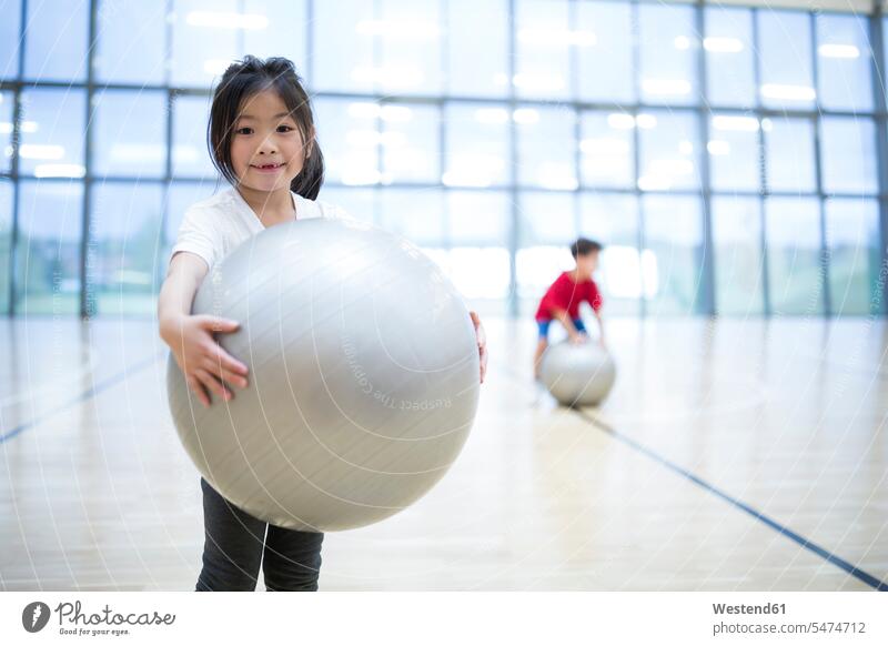 Porträt eines lächelnden Schulmädchens, das im Sportunterricht einen Gymnastikball hält Schule Schulen halten Fitnessball Sitzball Portrait Porträts Portraits