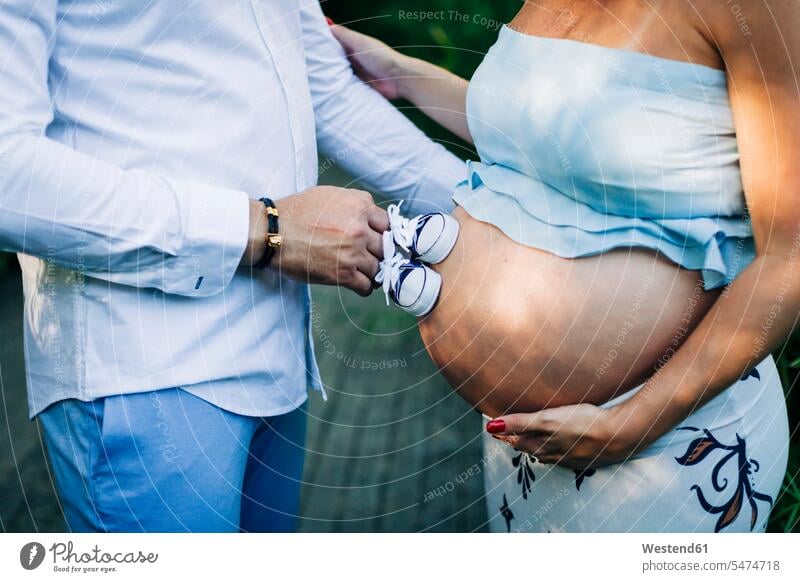 Mann berührt den Bauch einer schwangeren Frau mit Babyschuhen Farbaufnahme Farbe Farbfoto Farbphoto Außenaufnahme außen draußen im Freien Tag Tageslichtaufnahme