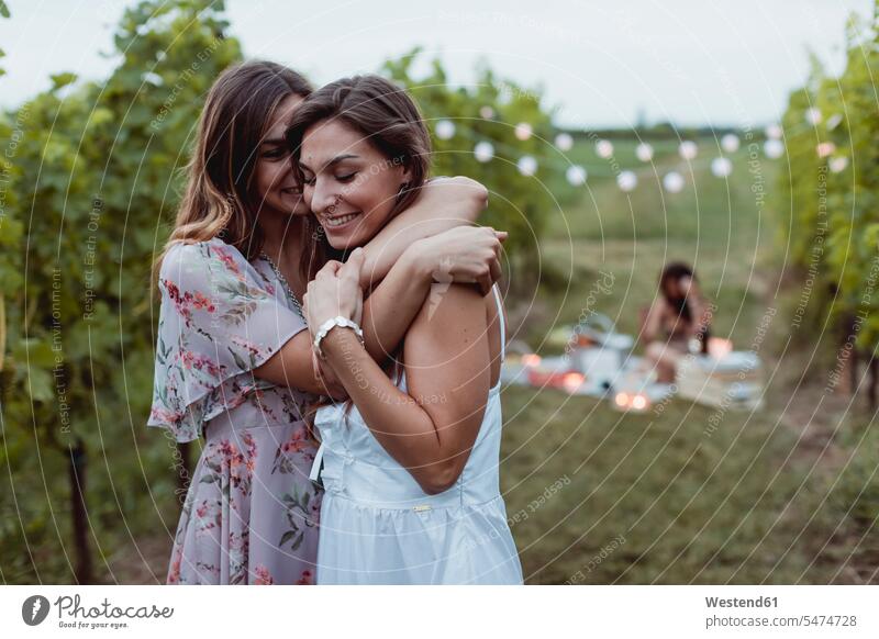 Zwillingsschwestern umarmen sich beim sommerlichen Picknick in einem Weinberg Umarmung Umarmungen Arm umlegen Freundinnen beschwipst Weingaerten Weingarten