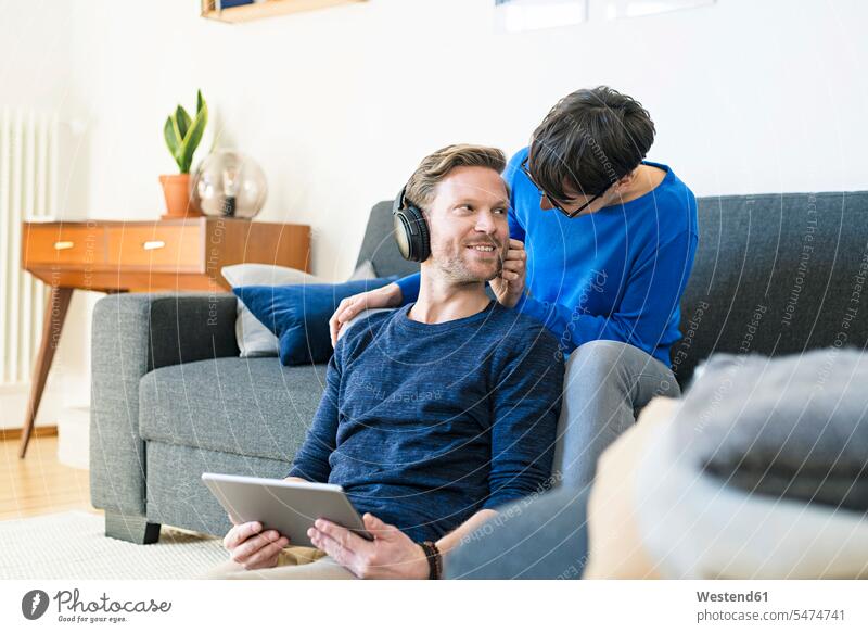 Lässiges Paar mit Kopfhörern entspannt auf der Lounge-Couch in ihrem modernen Wohnzimmer Sofa Couches Liege Sofas Tablet Tablet Computer Tablet-PC Tablet PC