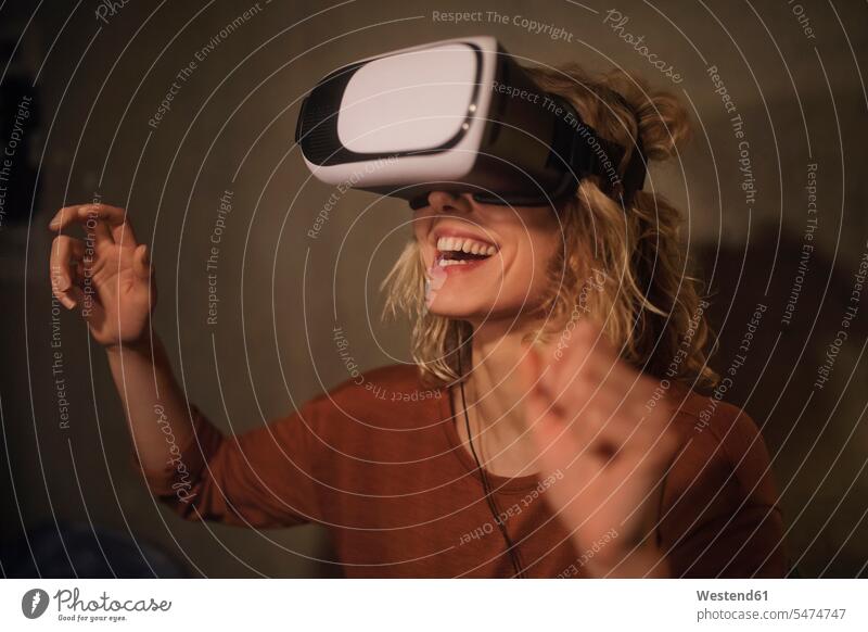 Lachende junge Frau benutzt zu Hause eine Virtual-Reality-Brille entdecken schauen Begeisterung entspannt Freude Zuhause neu Erfahrung Erlebnis erkunden
