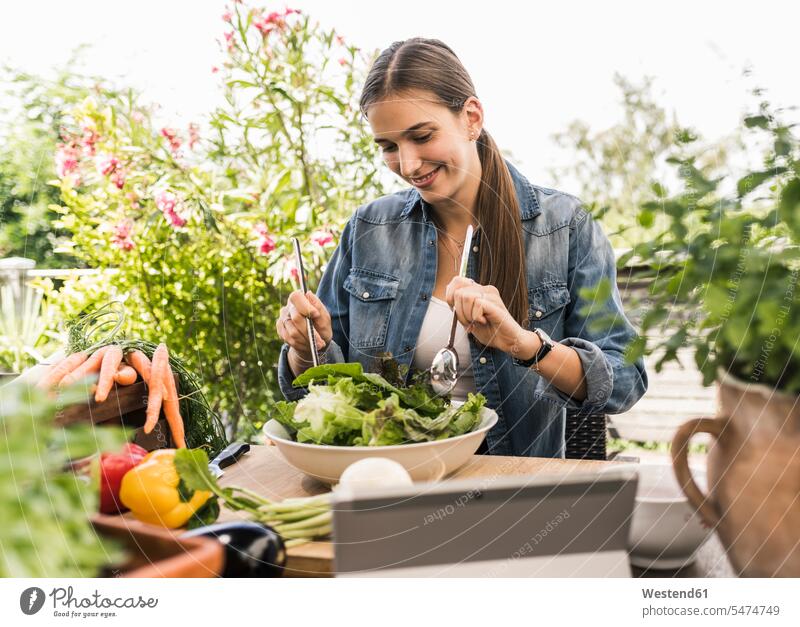 Lächelnde junge Frau bereitet Salat auf dem Tisch im Hof zu Farbaufnahme Farbe Farbfoto Farbphoto Deutschland Freizeitbeschäftigung Muße Zeit Zeit haben
