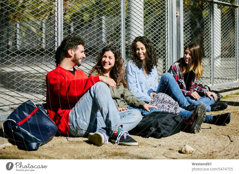 Vier glückliche Freunde sitzen am Zaun und unterhalten sich sitzend sitzt Glück glücklich sein glücklichsein Gruppe Gruppe von Menschen Menschengruppe sprechen