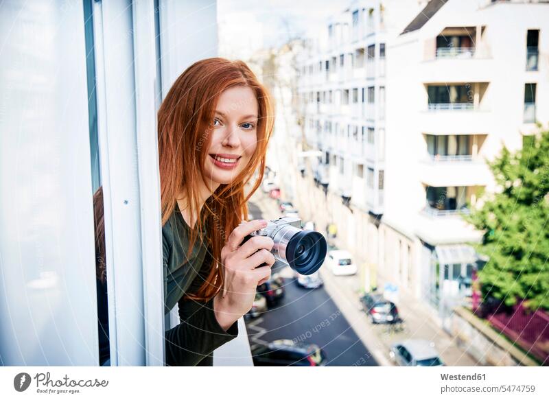 Porträt einer lächelnden rothaarigen Frau mit aus dem Fenster gelehnter Kamera Fotoapparat Fotokamera Portrait Porträts Portraits weiblich Frauen rote Haare