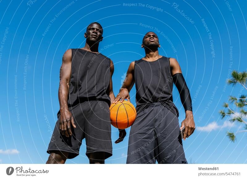 Junge Männer halten Basketball auf Basketballfeld Leute Menschen People Person Personen Afrikanisch Afrikanische Abstammung dunkelhäutig Farbige Farbiger