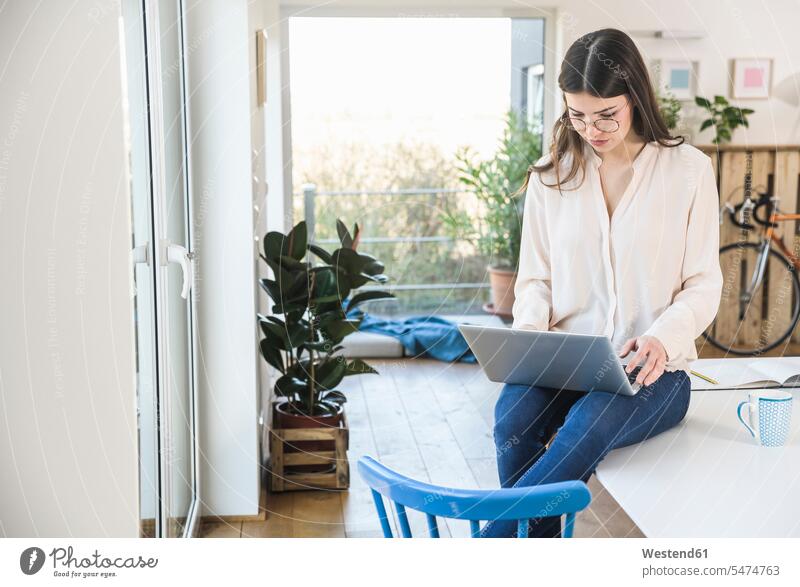 Junge Frau sitzt auf dem Tisch zu Hause mit Laptop Notebook Laptops Notebooks weiblich Frauen Zuhause daheim Tische sitzen sitzend Computer Rechner Erwachsener