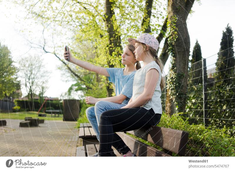 Zwei Mädchen sitzen auf einer Parkbank und machen ein Selfie Leute Menschen People Person Personen Europäisch Kaukasier kaukasisch 2 2 Menschen 2 Personen zwei
