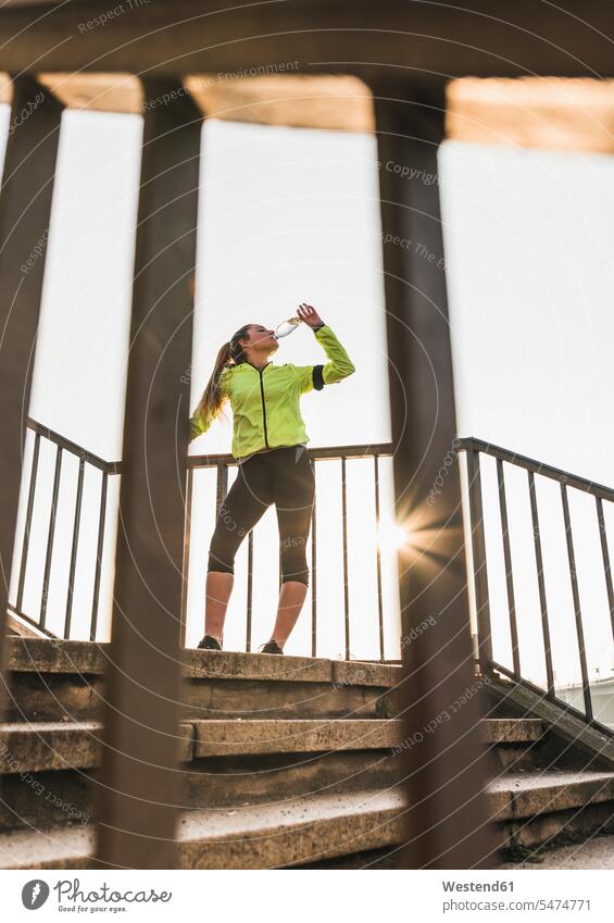 Sportliche junge Frau steht auf einer Treppe und trinkt aus der Flasche stehen stehend sportlich Flaschen weiblich Frauen Treppenaufgang trinken Erwachsener