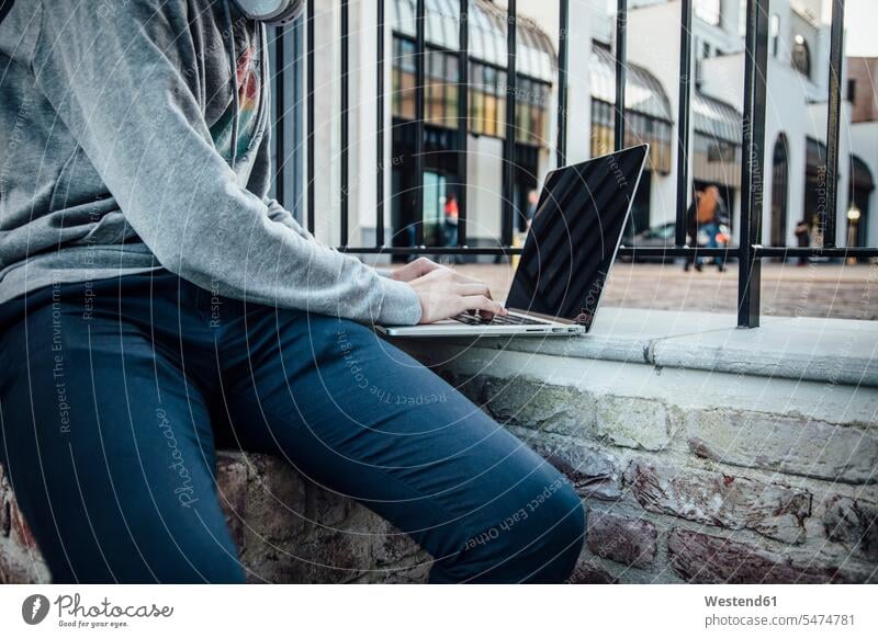 Teenager mit Laptop in der Stadt Zäune Kopfhoerer Rechner Laptops Notebook Notebooks sitzend sitzt Muße Individuell Technik Technologien mobil außen draußen