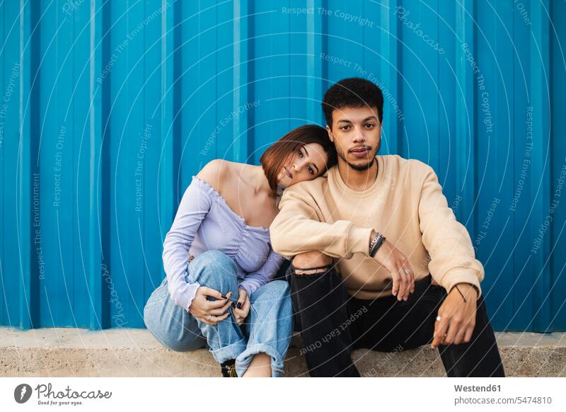 Freundin lehnt auf Freund Schulter, während gegen blaue Wand sitzen Farbaufnahme Farbe Farbfoto Farbphoto Außenaufnahme außen draußen im Freien Tag