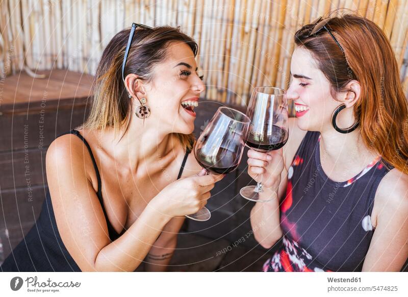 Zwei glückliche Frauen mit einem Glas Rotwein an einer Bar Freunde Kameradschaft Freundin Gläser Trinkglas Trinkgläser sitzend sitzt reden sommerlich Sommerzeit
