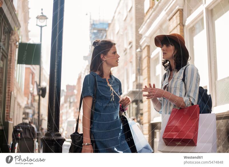 Schöne Freundinnen unterhalten sich im Stehen mit Einkaufstaschen in der Stadt Farbaufnahme Farbe Farbfoto Farbphoto Außenaufnahme außen draußen im Freien Tag