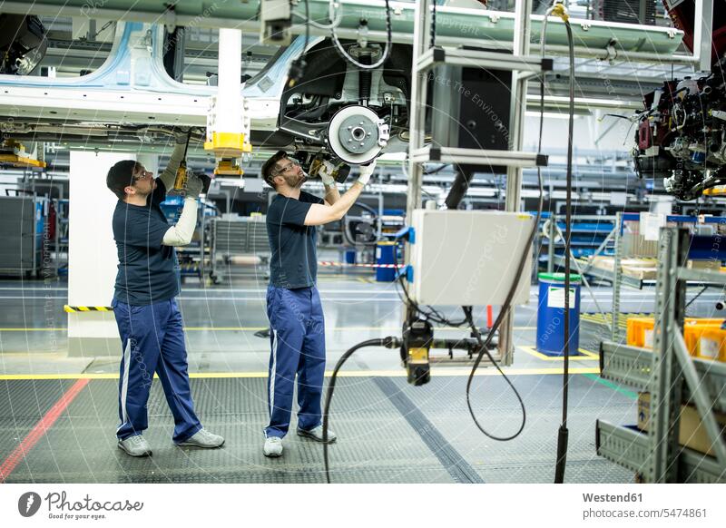 Zwei Kollegen arbeiten am Autounterboden in einer modernen Fabrik Arbeitskollege Arbeitskollegen Job Berufe Berufstätigkeit Beschäftigung Jobs Arbeiter T-Shirts