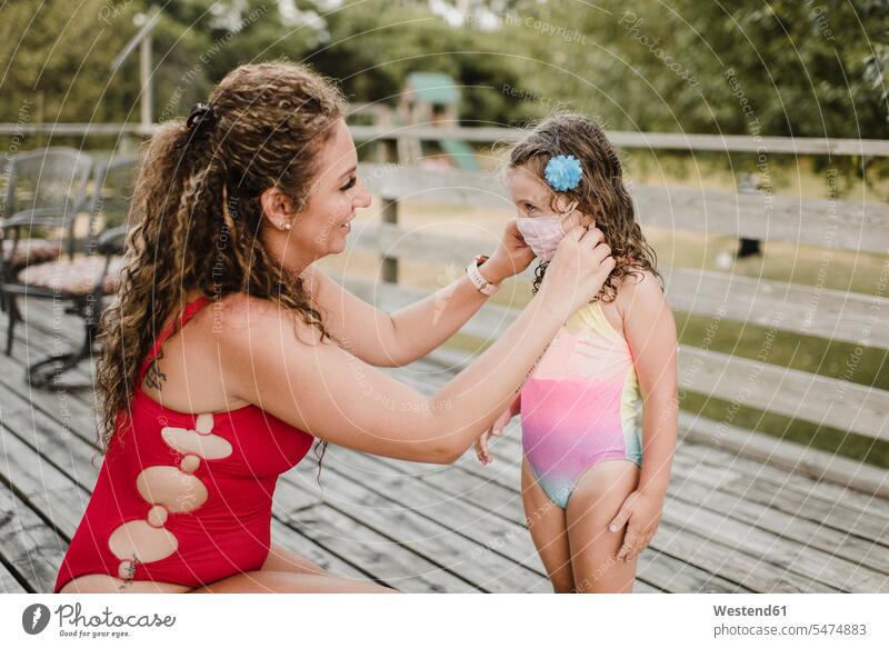 Mutter im Badeanzug trägt schützende Gesichtsmaske auf Tochter Leute Menschen People Person Personen Europäisch Kaukasier kaukasisch 2 2 Menschen 2 Personen