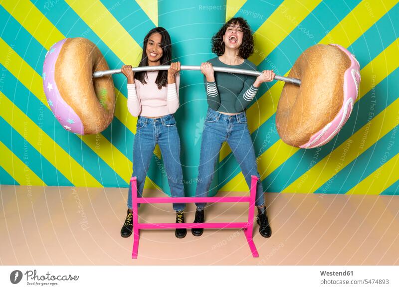Zwei glückliche junge Frauen in einem Indoor-Vergnügungspark haben Spaß mit übergroßen Donuts Spanien Doughnut Doughnuts verspielt spielerisch offenes Lächeln