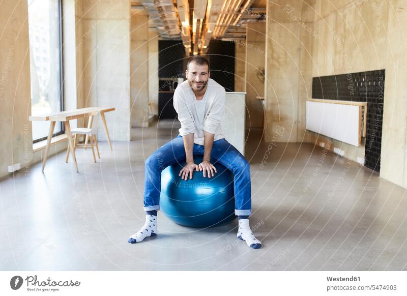 Porträt eines jungen Mannes, der auf einem Fitnessball in einem modernen Büro sitzt Deutschland Gymnastikball Sitzball Freiberufler freiberuflich freie Berufe