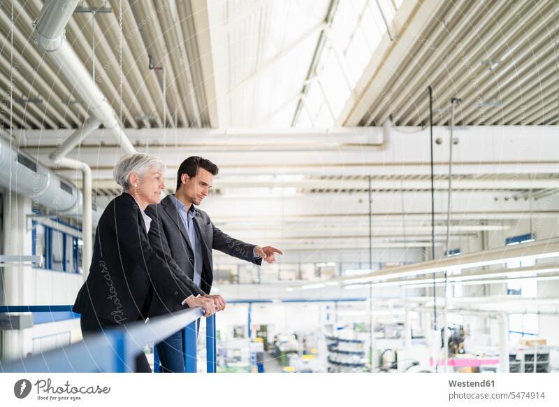 Ältere Geschäftsfrau und Geschäftsmann im Obergeschoss einer Fabrik mit Blick auf den Verkaufsraum überblicken oberes Stockwerk Fabriken Produktionshalle