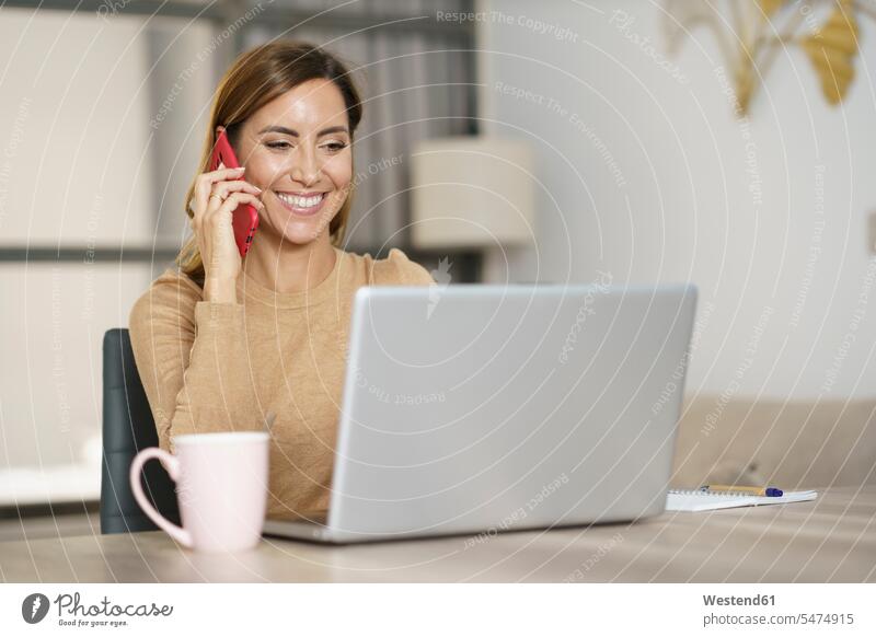 Geschäftsfrau lächelt beim Telefonieren zu Hause Farbaufnahme Farbe Farbfoto Farbphoto Innenaufnahme Innenaufnahmen innen drinnen Tag Tageslichtaufnahme
