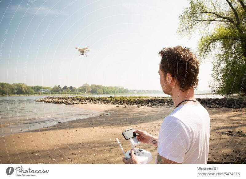 Mann fliegt Drohne an einem Fluss Fluesse Fluß Flüsse fliegen fliegend Drohnen Männer männlich Gewässer Wasser Erwachsener erwachsen Mensch Menschen Leute