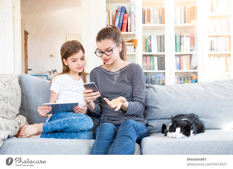 Zwei Schwestern sitzen zu Hause auf der Couch und benutzen elektronische Geräte Deutschland Tablet Tablet Computer Tablet-PC Tablet PC iPad Tablet-Computer