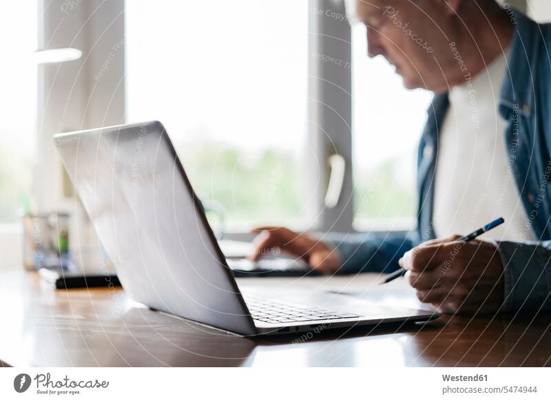 Älterer Mann benutzt Taschenrechner und Laptop beim Schreiben zu Hause Farbaufnahme Farbe Farbfoto Farbphoto Innenaufnahme Innenaufnahmen innen drinnen Tag
